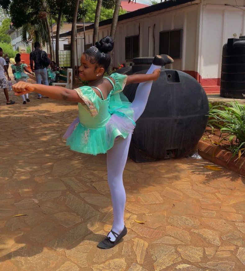 Young girl in ballet pose outdoors with school buildings in background